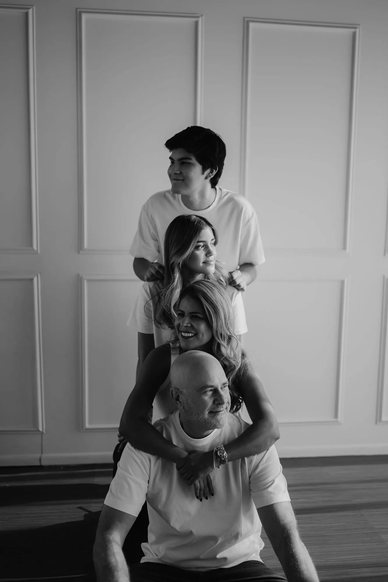 En blanco y negro, una familia apilada de pie, con el papá sentado abajo, frente a una pared con molduras.