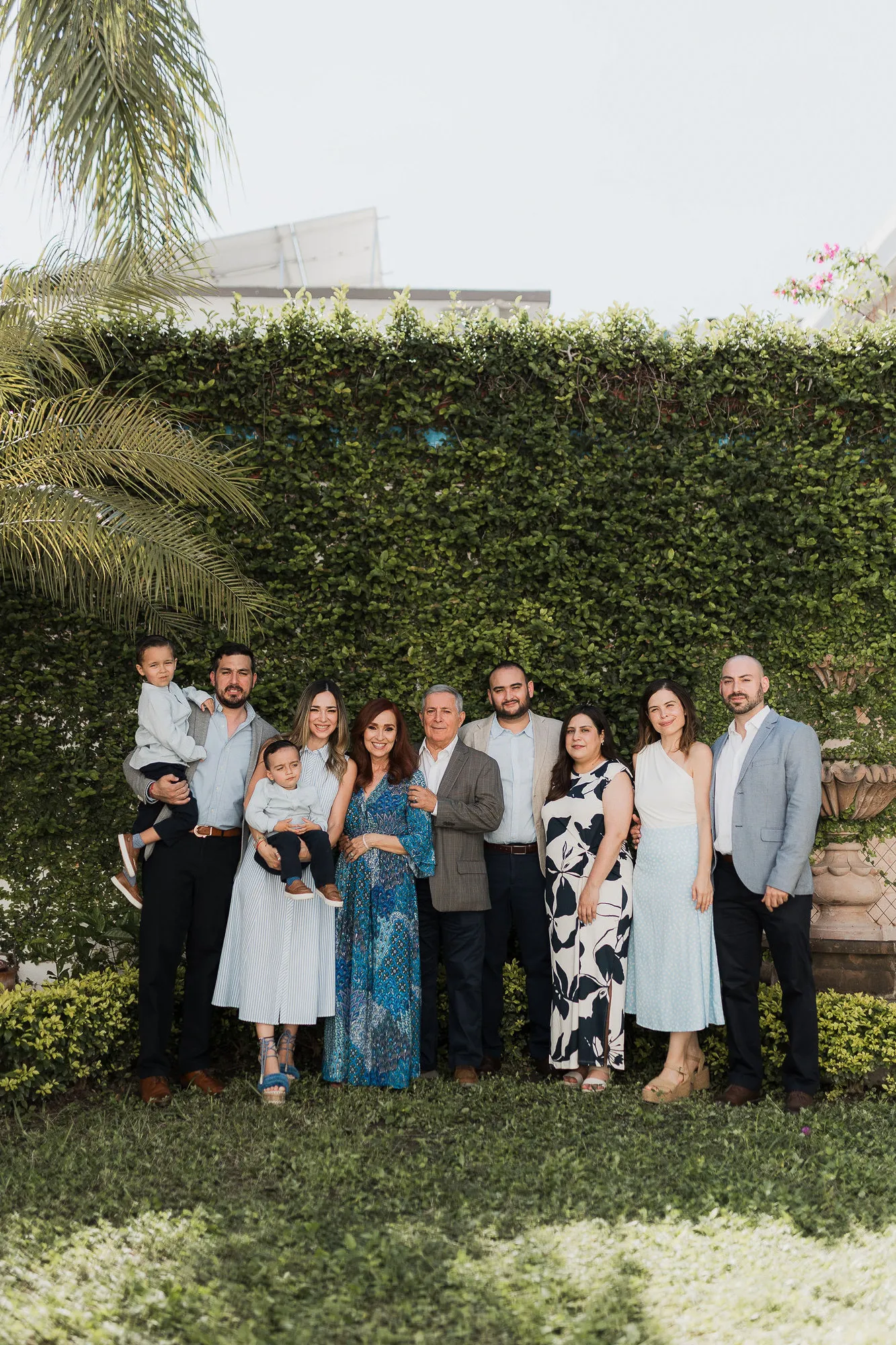 Una familia numerosa posa frente a un muro de plantas, en un jardín.
