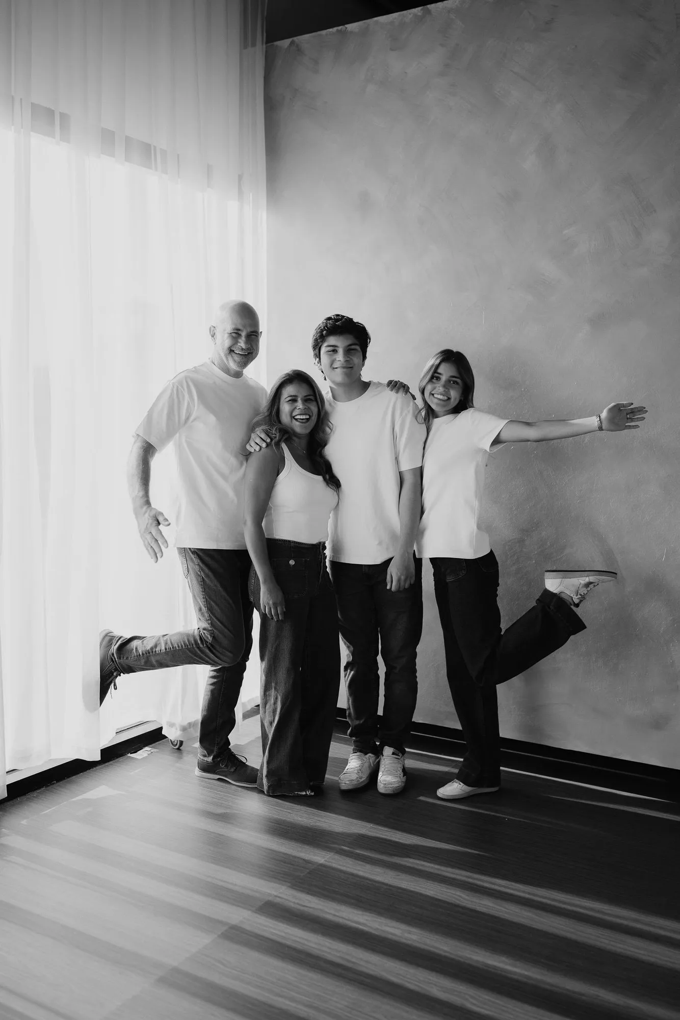 En blanco y negro, una familia posa de pie, de forma divertida, junto a una ventana.