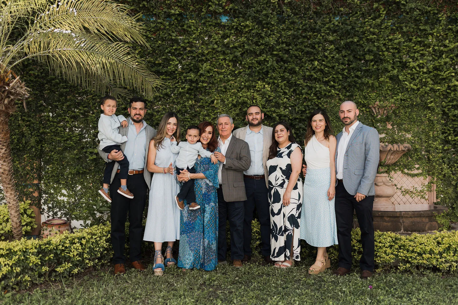 Una familia numerosa posa de pie en el jardín, frente a un muro de plantas.