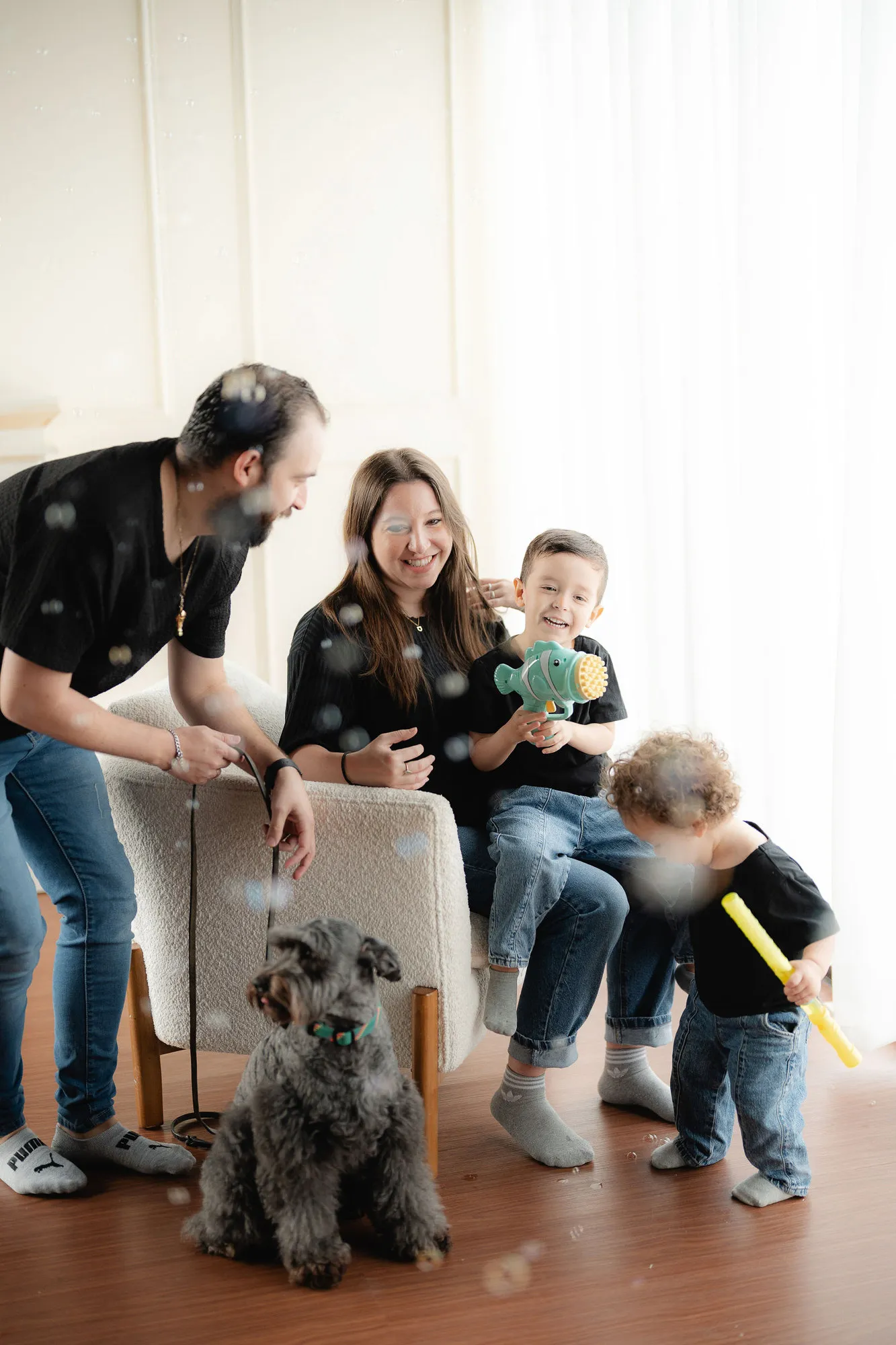 Una familia con niños y un perro se divierte en el estudio, junto a una cortina blanca.