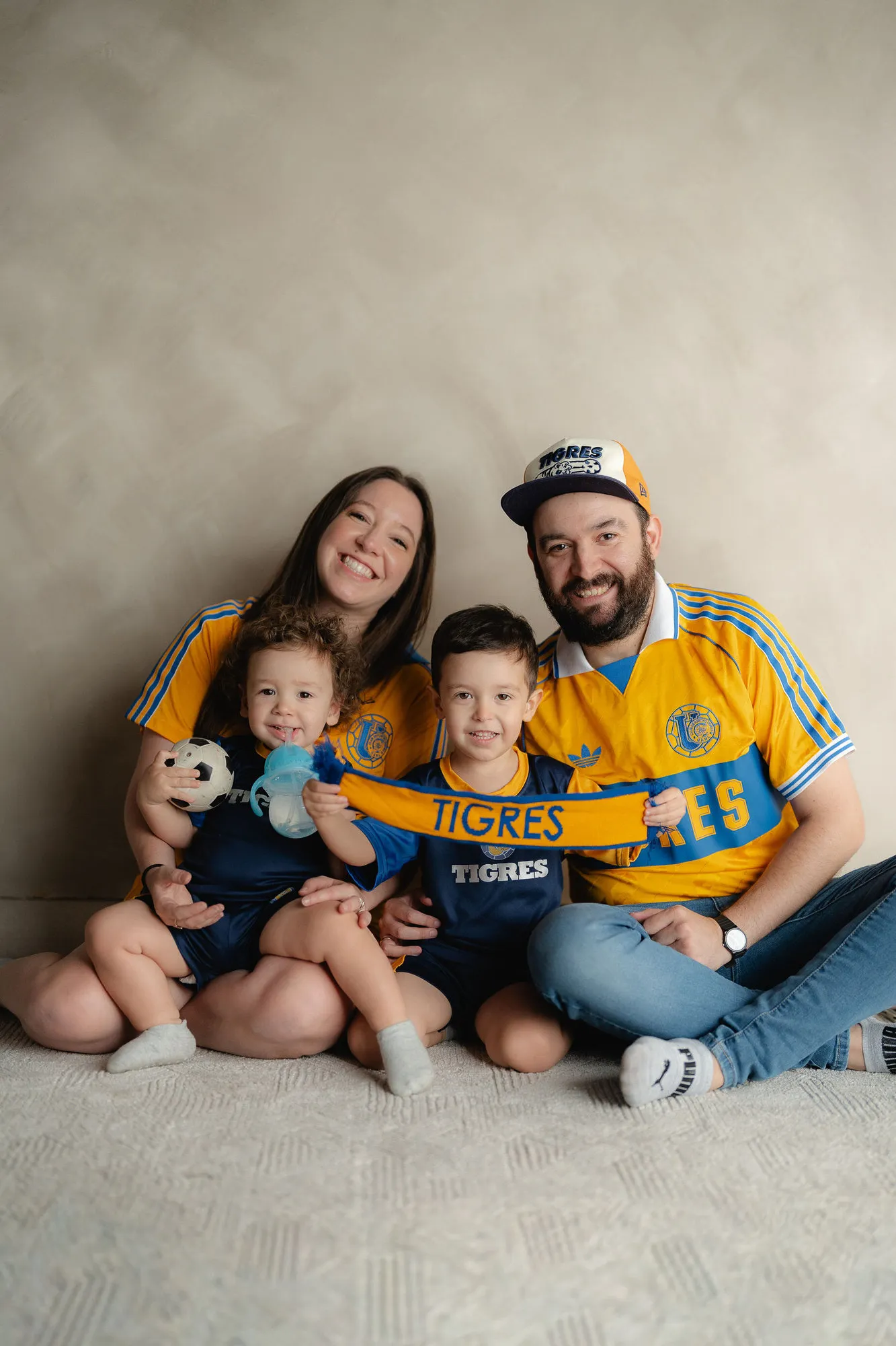 Una familia con jerseys amarillos de futbol sonríe sentada en el piso, con un perro.
