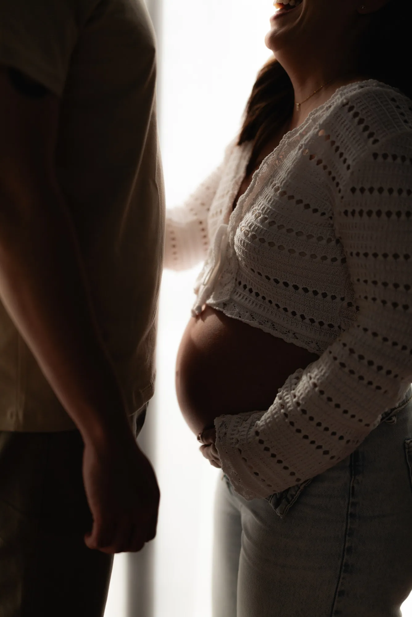 Detalle de una mujer embarazada con suéter tejido abierto, junto a su pareja.