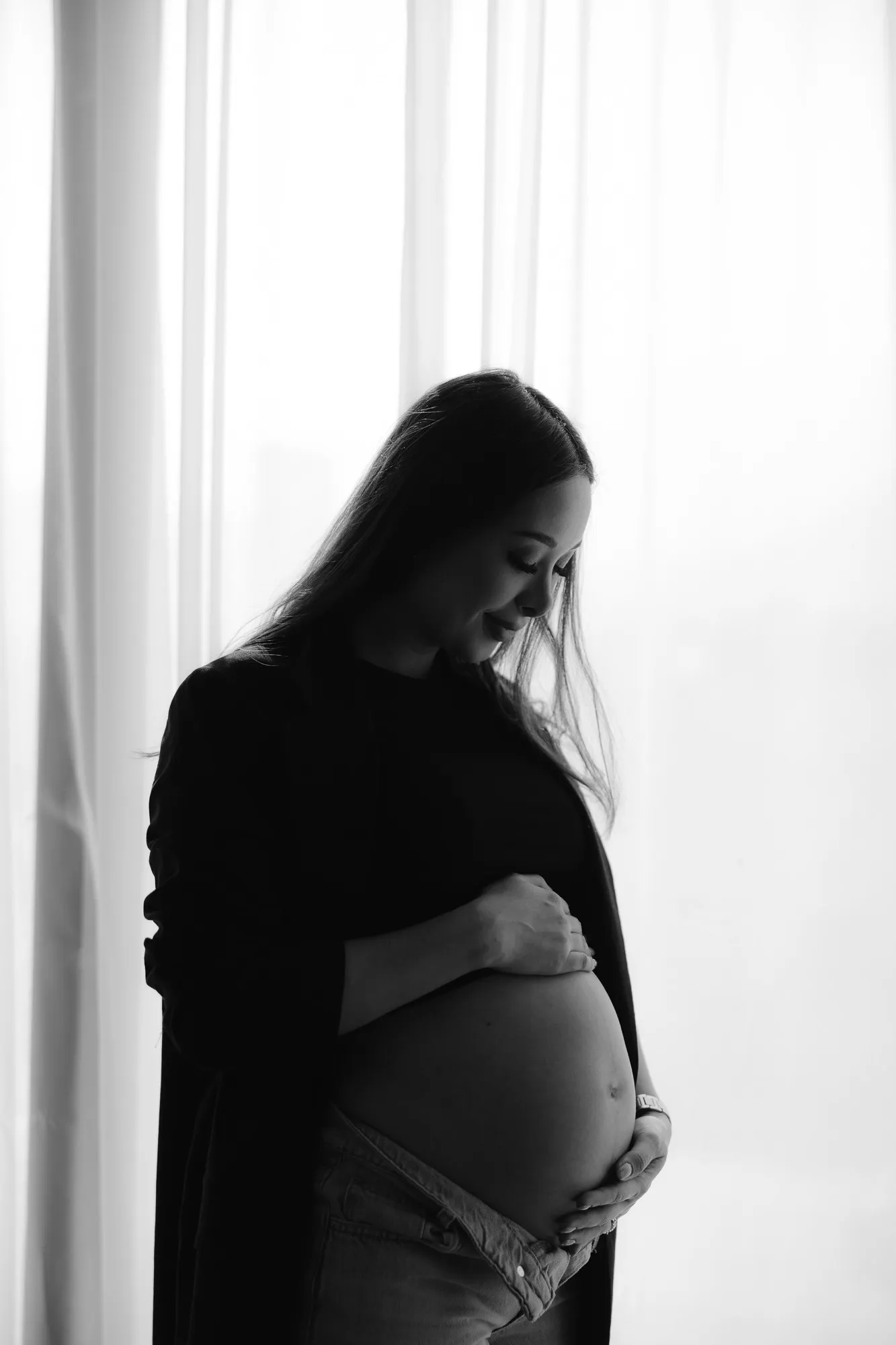 En blanco y negro, una mujer embarazada de perfil, a contraluz, con las manos en el vientre.