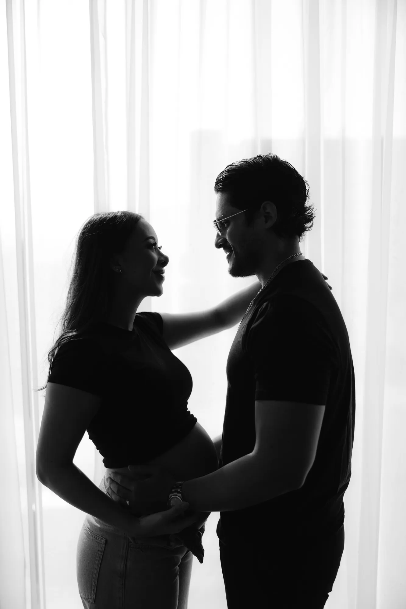 En blanco y negro, siluetas de una pareja frente a una ventana: se acercan y se toman por la cintura.