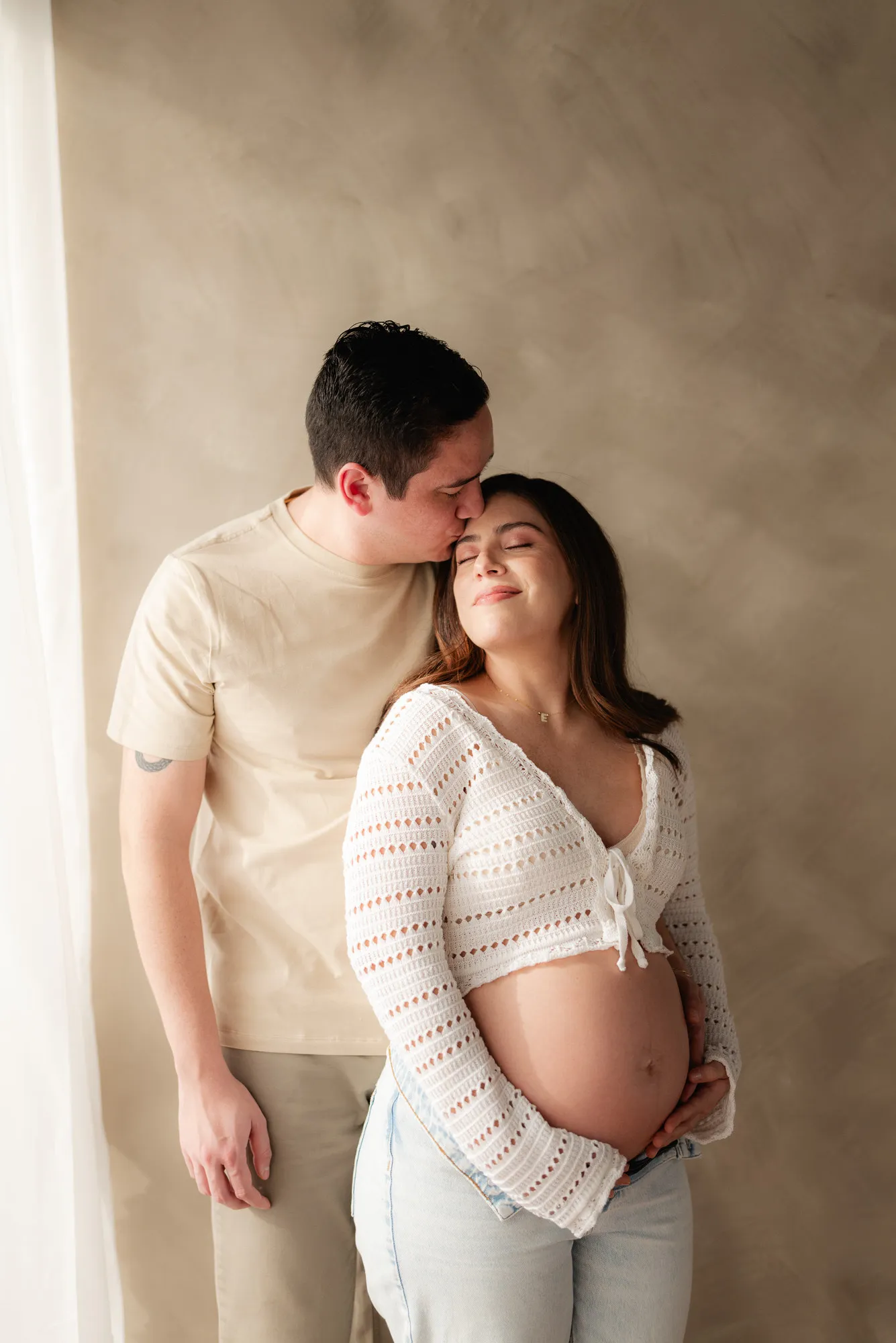 Una pareja se abraza; él besa la frente de ella, que lleva blusa tejida y jeans.
