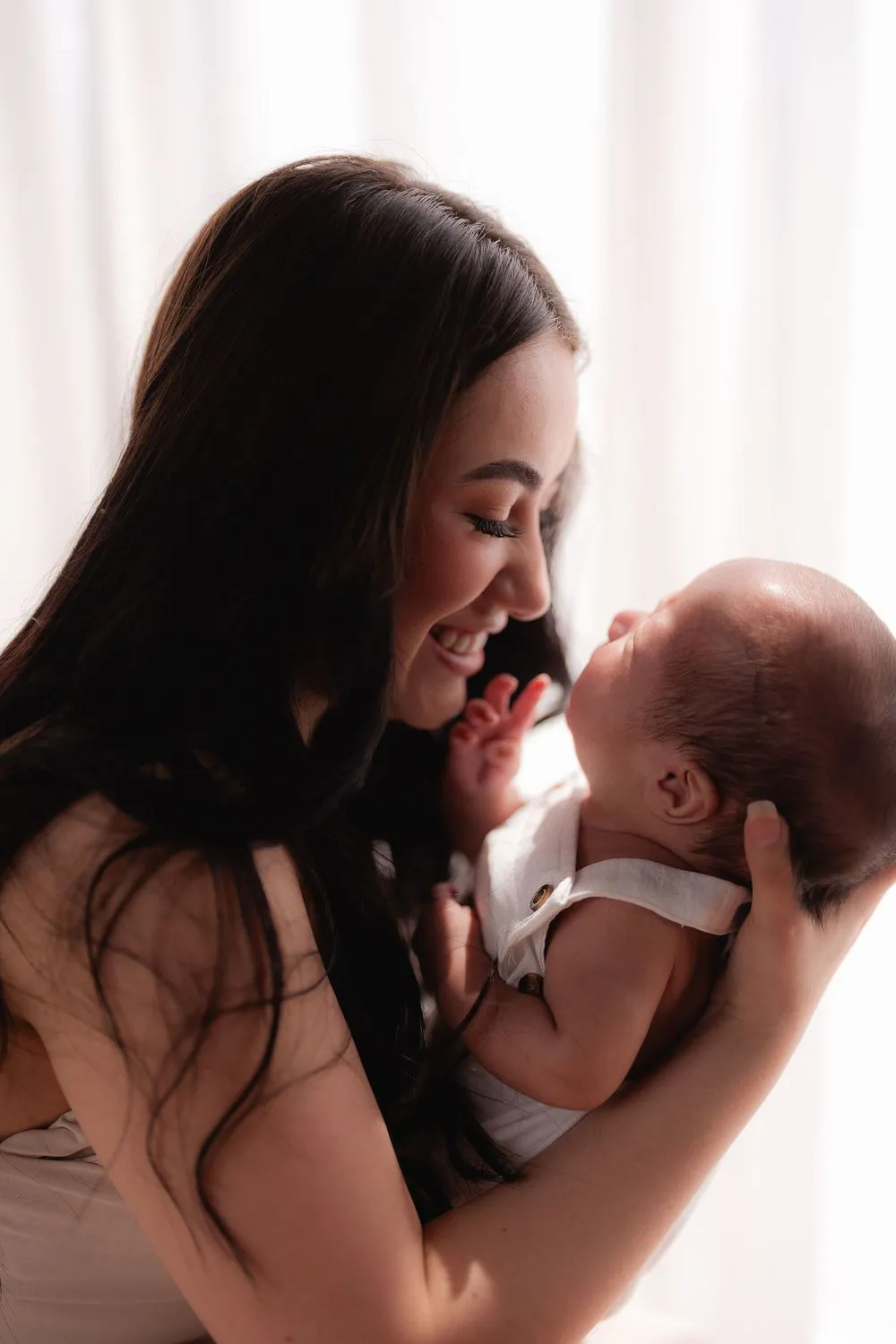 Una mamá sonríe y toca la nariz de su bebé, que sostiene en brazos.