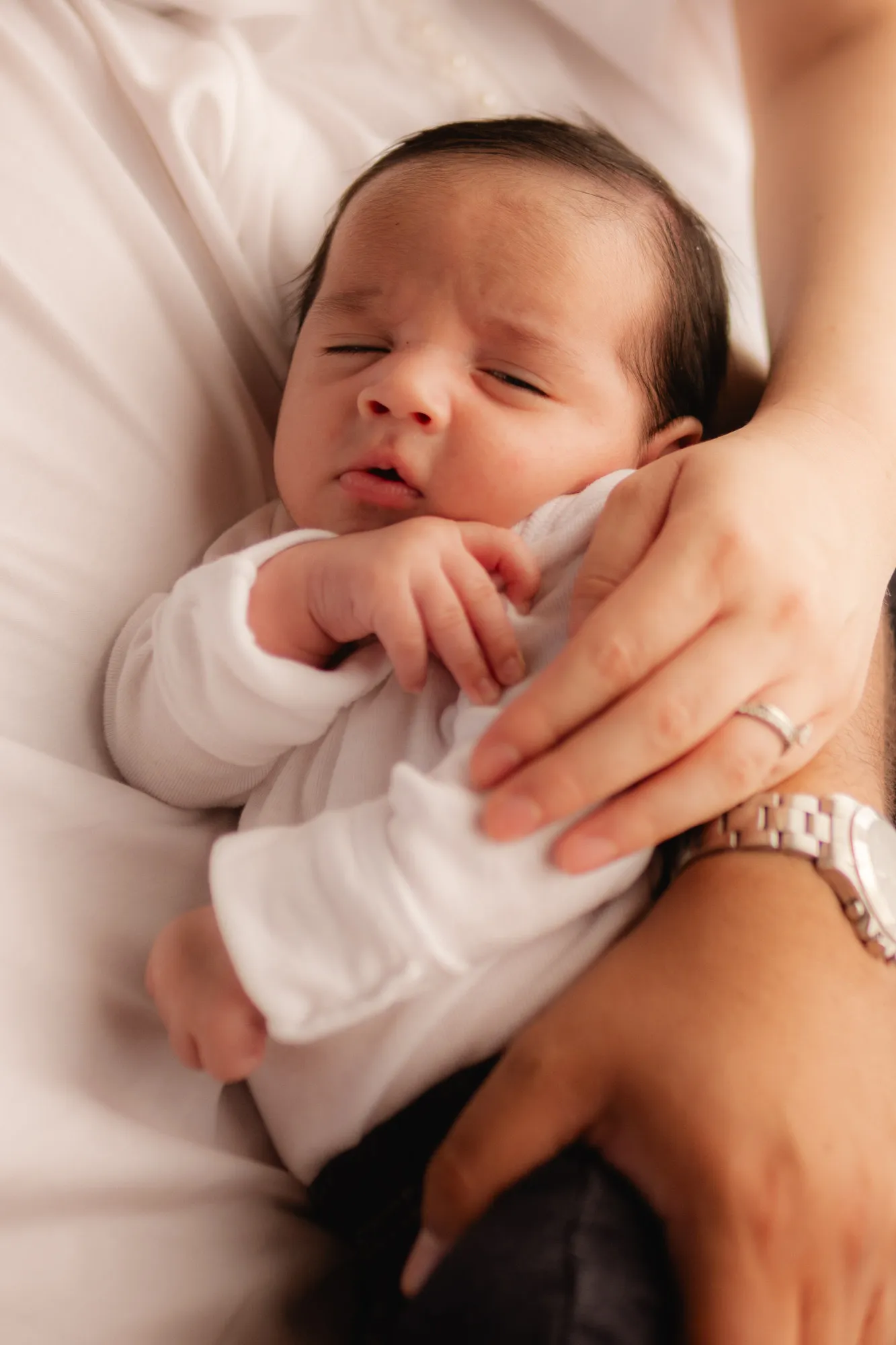 Un recién nacido dormido, sostenido por las manos de sus papás.