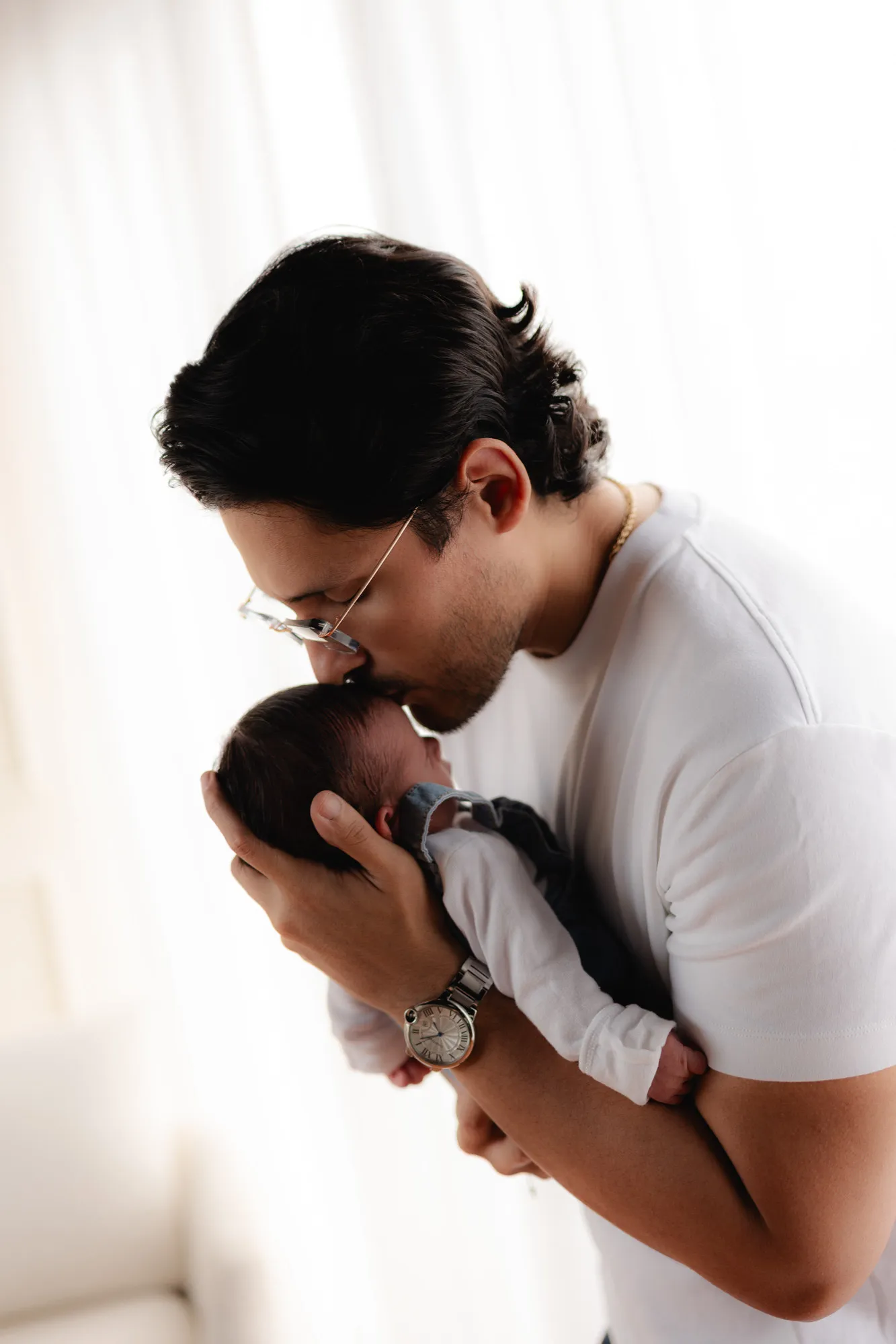 Un papá besa la cabeza de su bebé, que sostiene cerca de su pecho.
