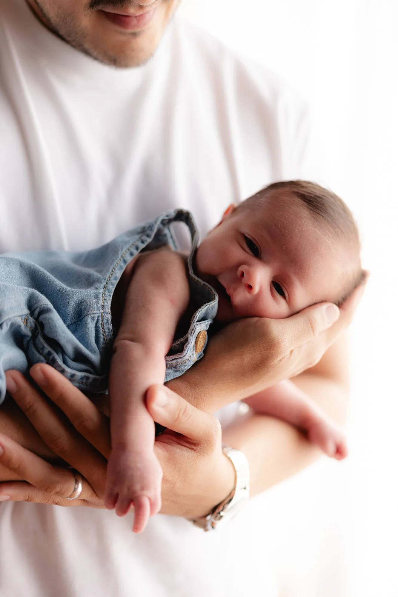 Un papá carga a su bebé dormido, con chaqueta de mezclilla.