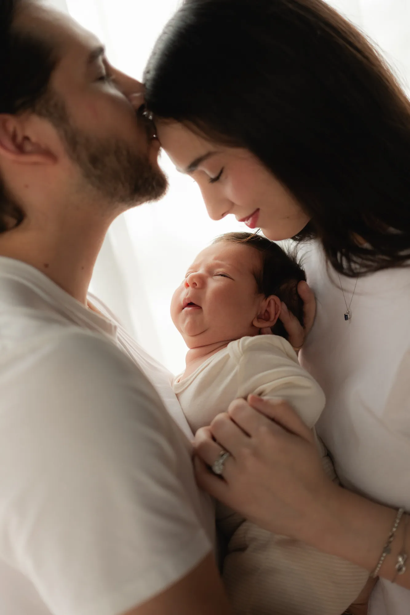 Un papá besa la frente de la mamá mientras sostienen a su bebé, que llora.