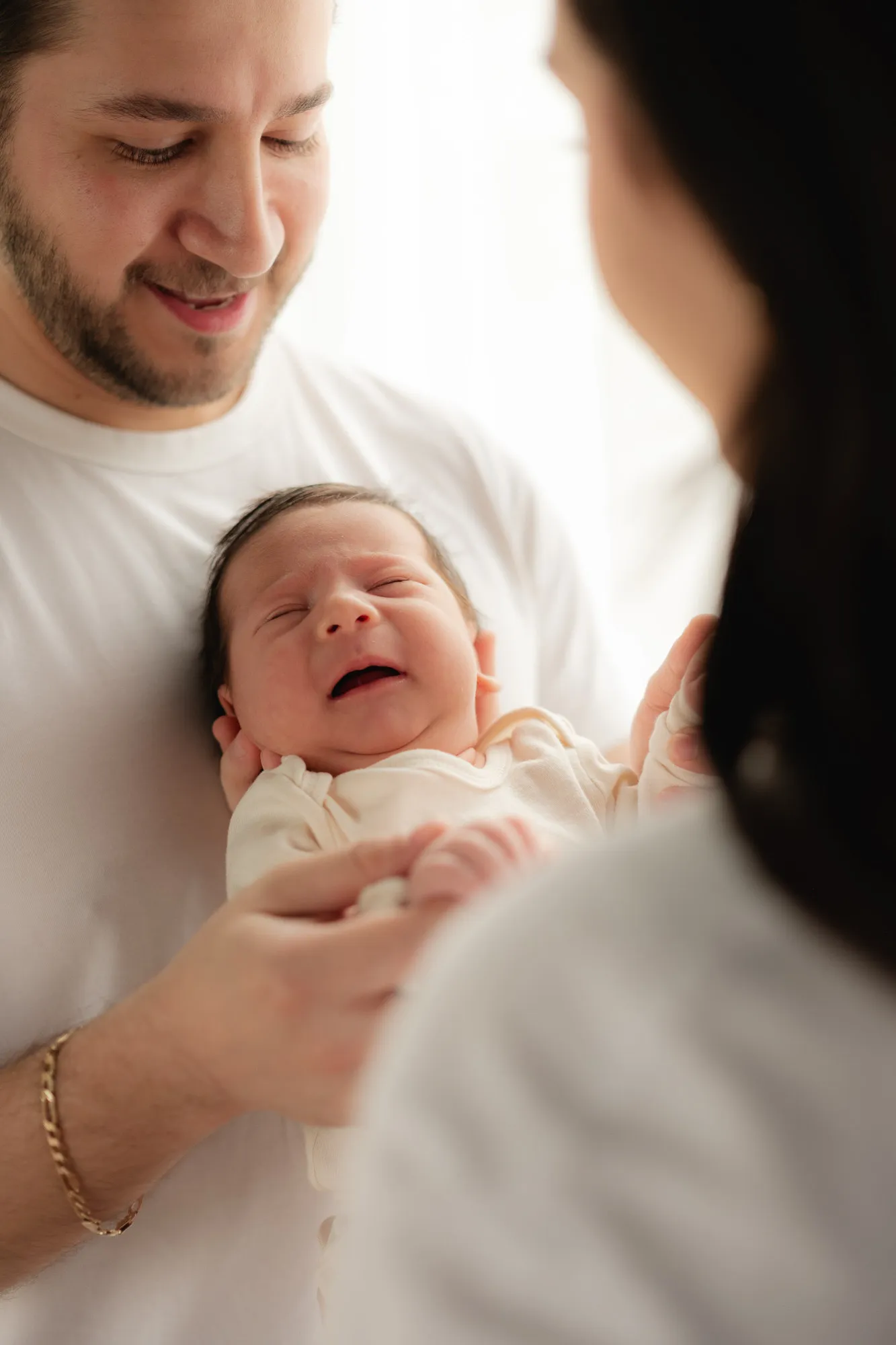 Un papá sonríe mientras carga a su bebé, que llora, junto a la mamá.