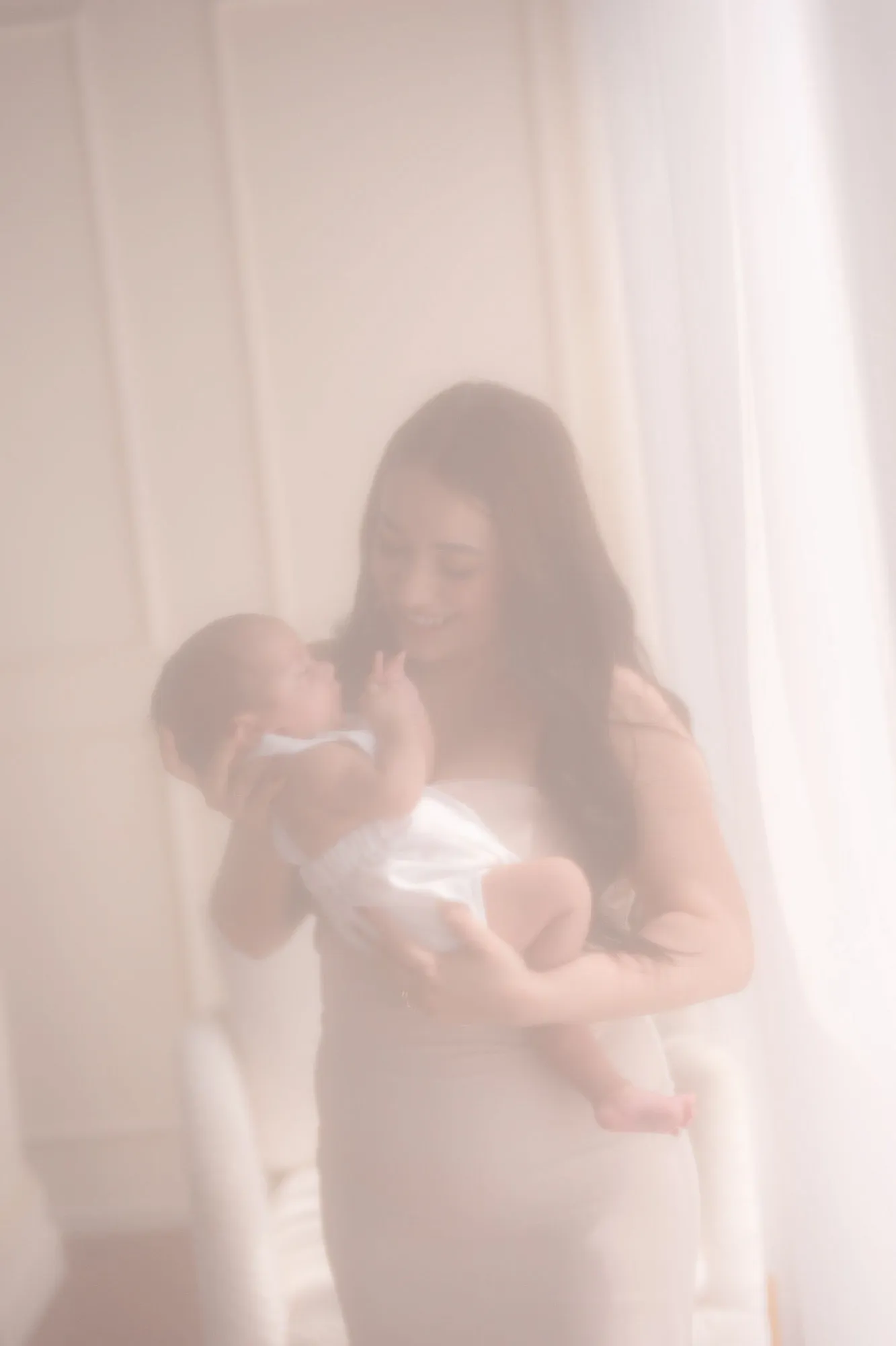 En una imagen suave y rosada, una mamá sostiene a su bebé.