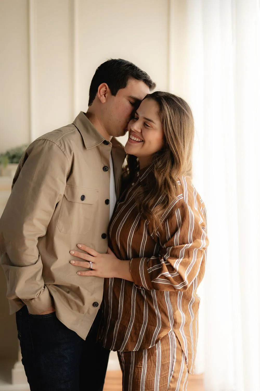 Una pareja se abraza sonriendo; él lleva una chamarra beige y ella una blusa de rayas.