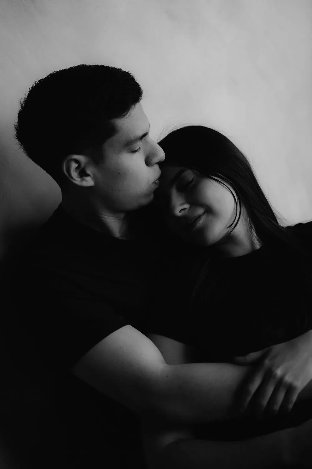 En blanco y negro, una pareja se abraza; él cierra los ojos y apoya la cara en la cabeza de ella.