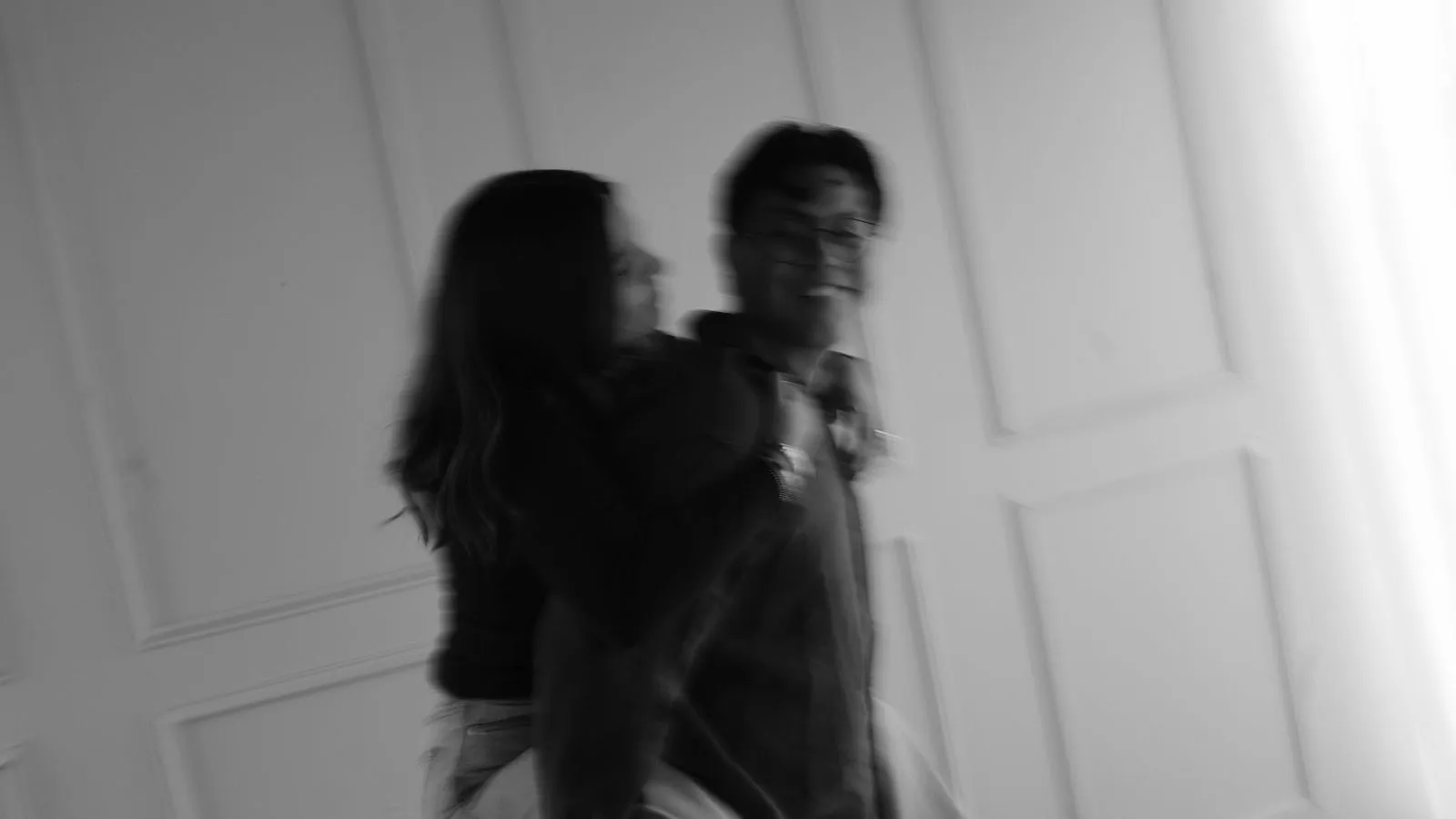 En blanco y negro, una pareja se abraza en movimiento, con la imagen desenfocada, frente a una puerta blanca.