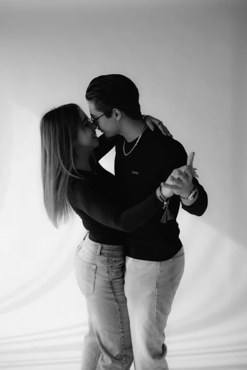 En blanco y negro, una pareja se besa mientras baila frente a un fondo blanco.