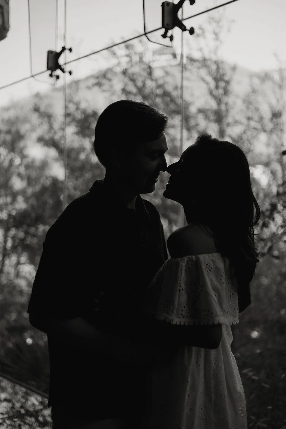 En blanco y negro, la silueta de una pareja a punto de besarse, con árboles y montañas al fondo.