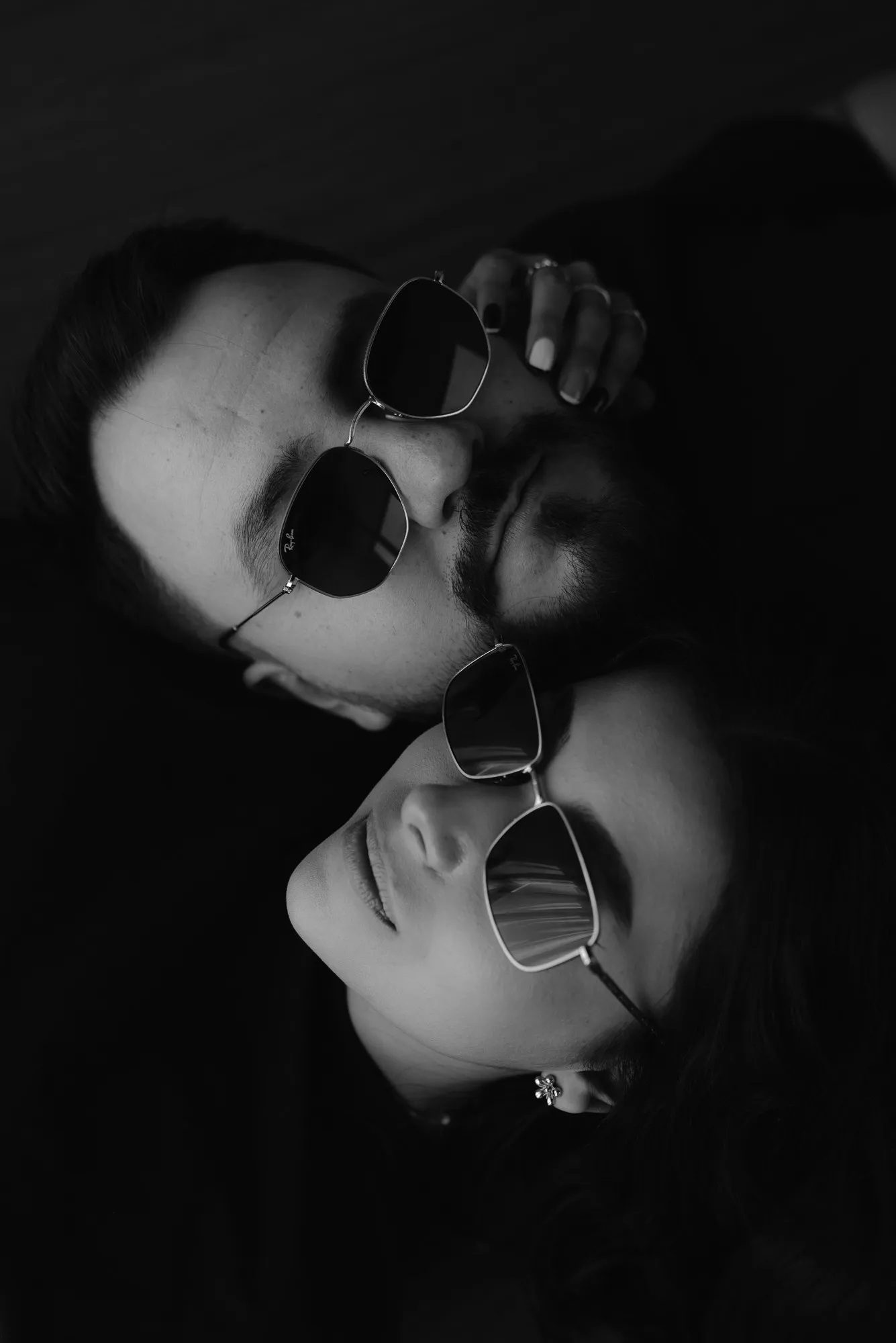 En blanco y negro, primer plano de dos personas recostadas con lentes de sol.