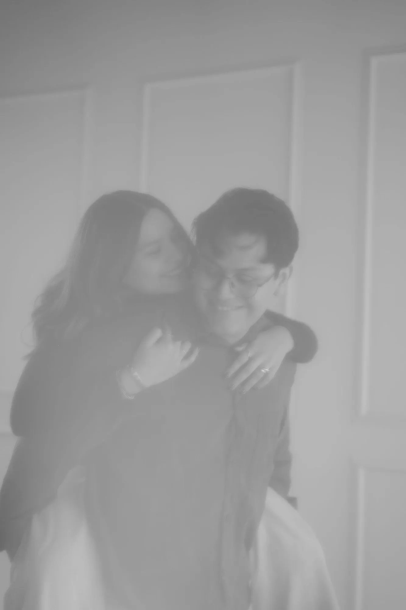 En blanco y negro, con un tono suave y desvanecido, una pareja se abraza.