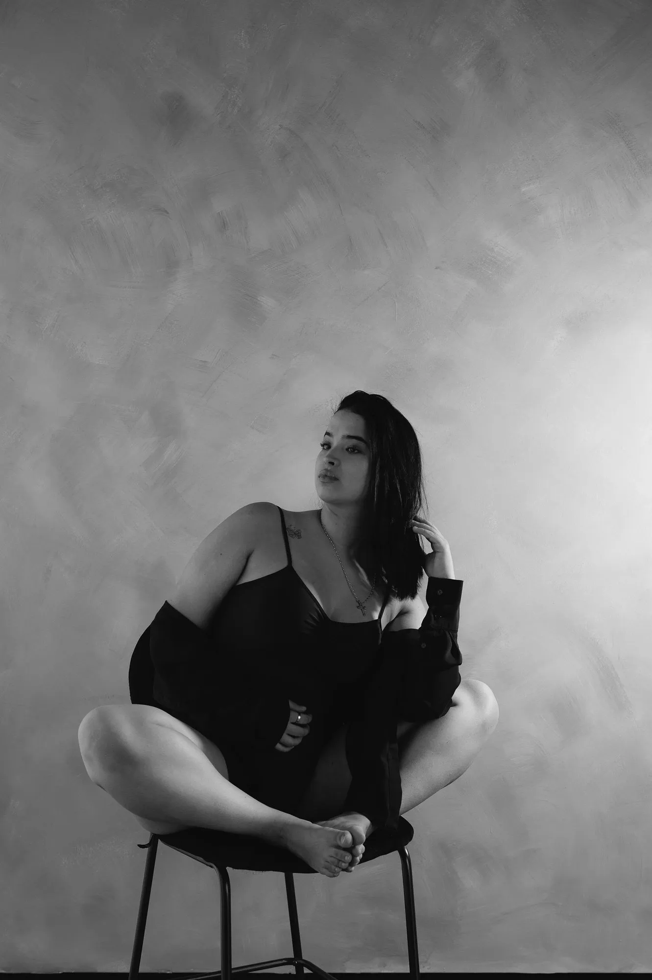 En blanco y negro, una mujer vestida de negro, sentada en un banco con las piernas cruzadas.