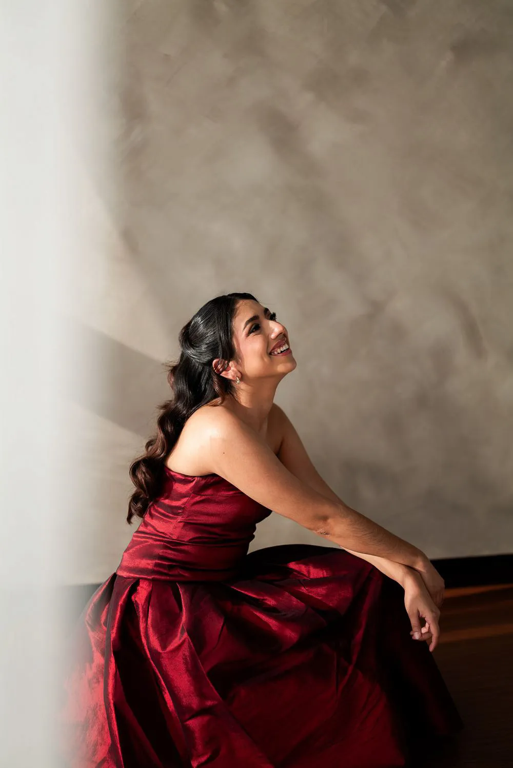 Una mujer con vestido rojo, sentada, mira hacia arriba y sonríe.
