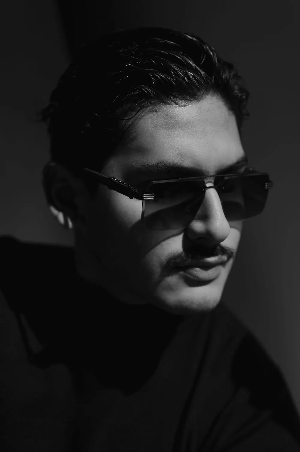 En blanco y negro, retrato de un hombre con lentes oscuros y bigote.