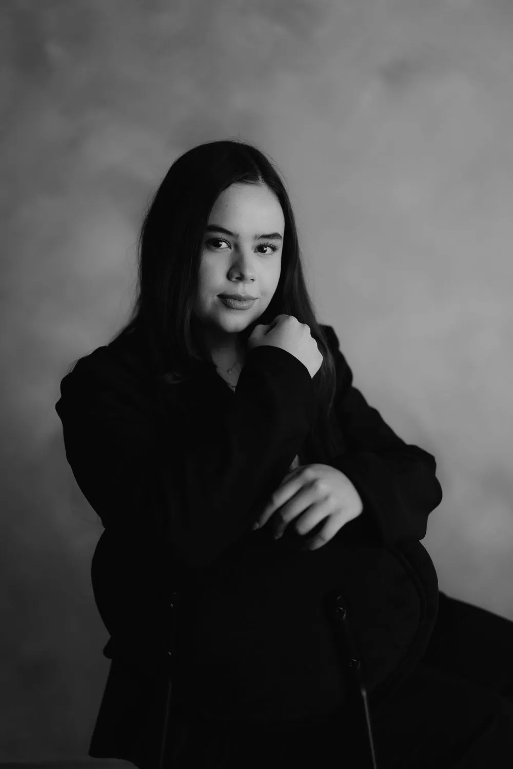 En blanco y negro, una mujer con saco oscuro mira de frente, sentada y con las manos juntas.