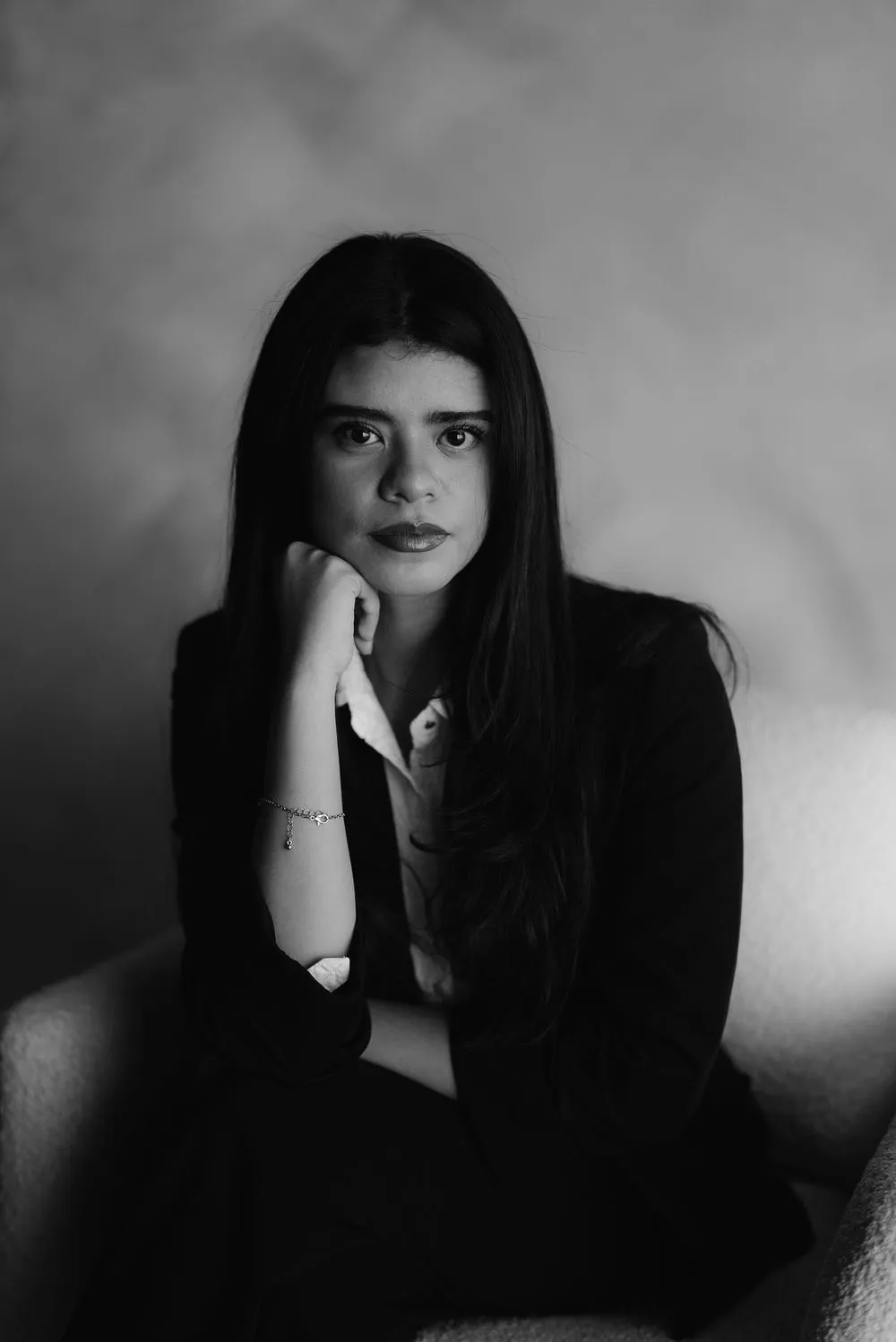 En blanco y negro, una mujer de cabello largo apoya la barbilla en la mano y mira a la cámara.