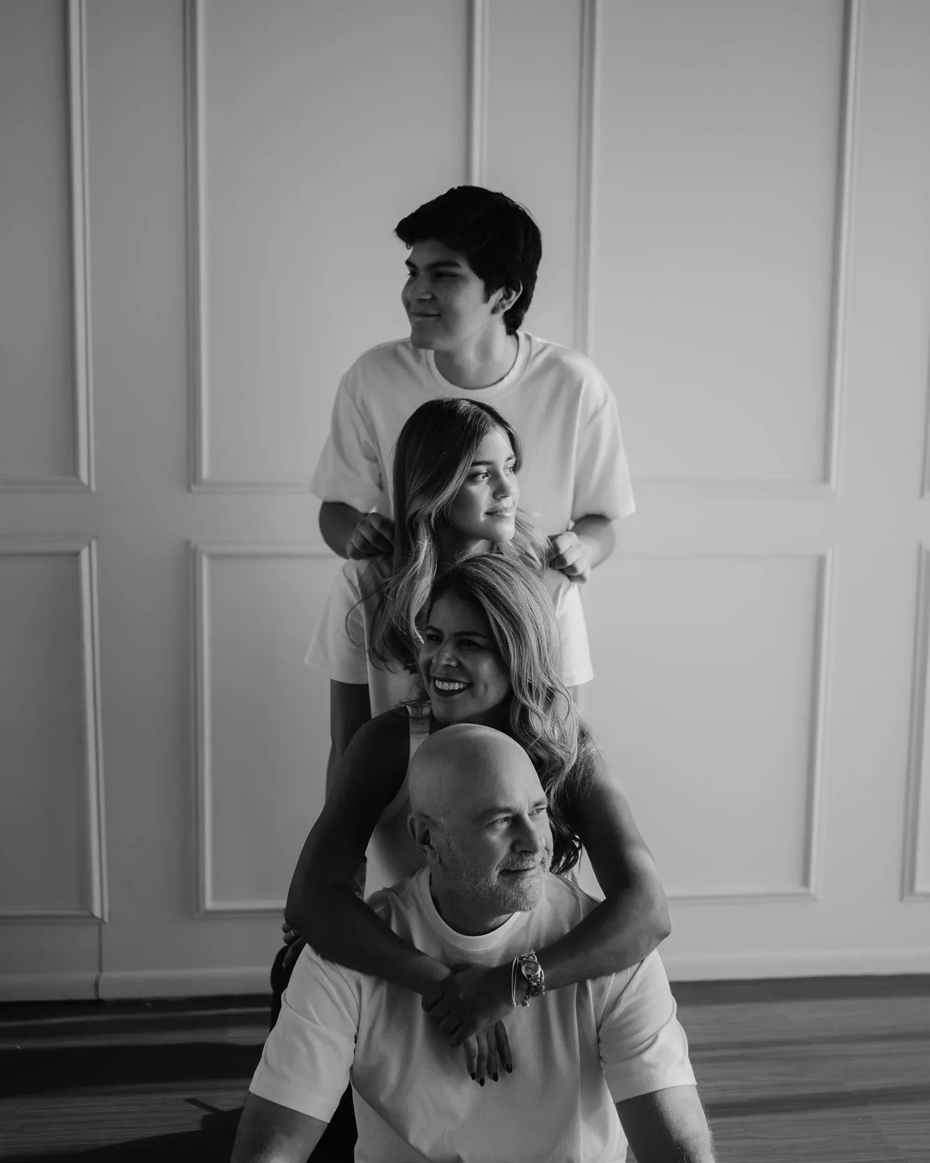 En blanco y negro, una familia apilada de pie, con el papá sentado abajo, frente a una pared con molduras.